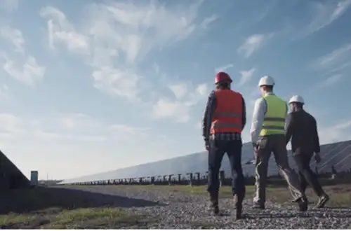 Three men walking along solar panels - Energy Image Three men walking along solar panels - Energy Image